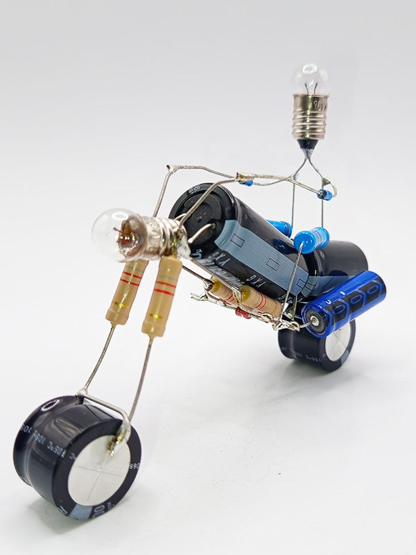 Une figurine en forme de moto de type chopper, fabriquée à partir de composants électroniques tels que des condensateurs, des résistances et des petites ampoules